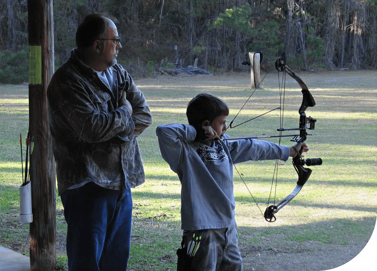 Boy aiming compound bow under supervision