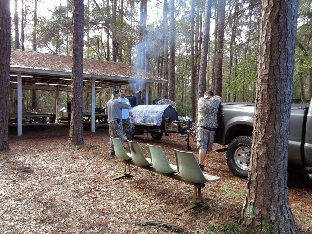 Man working on a plow attached to a truck in a wooded area.