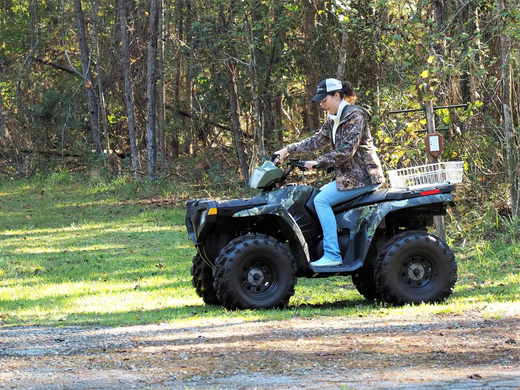 Person riding an ATV on a trail through a wooded area.