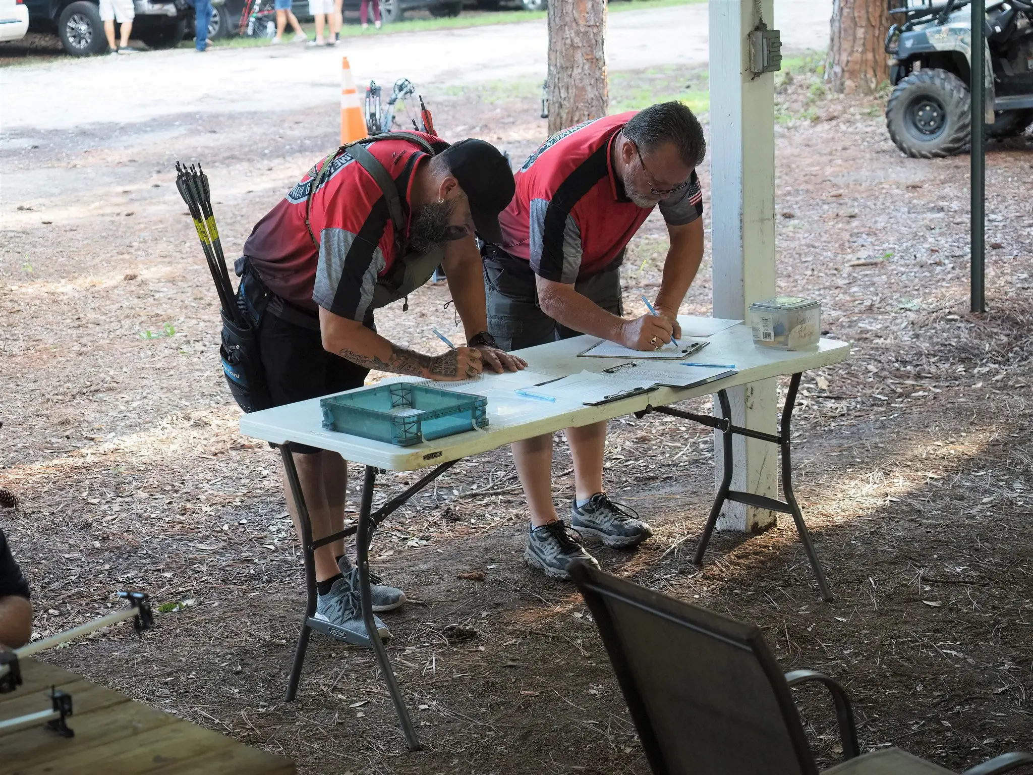 Two men filling out forms on a table outdoors.