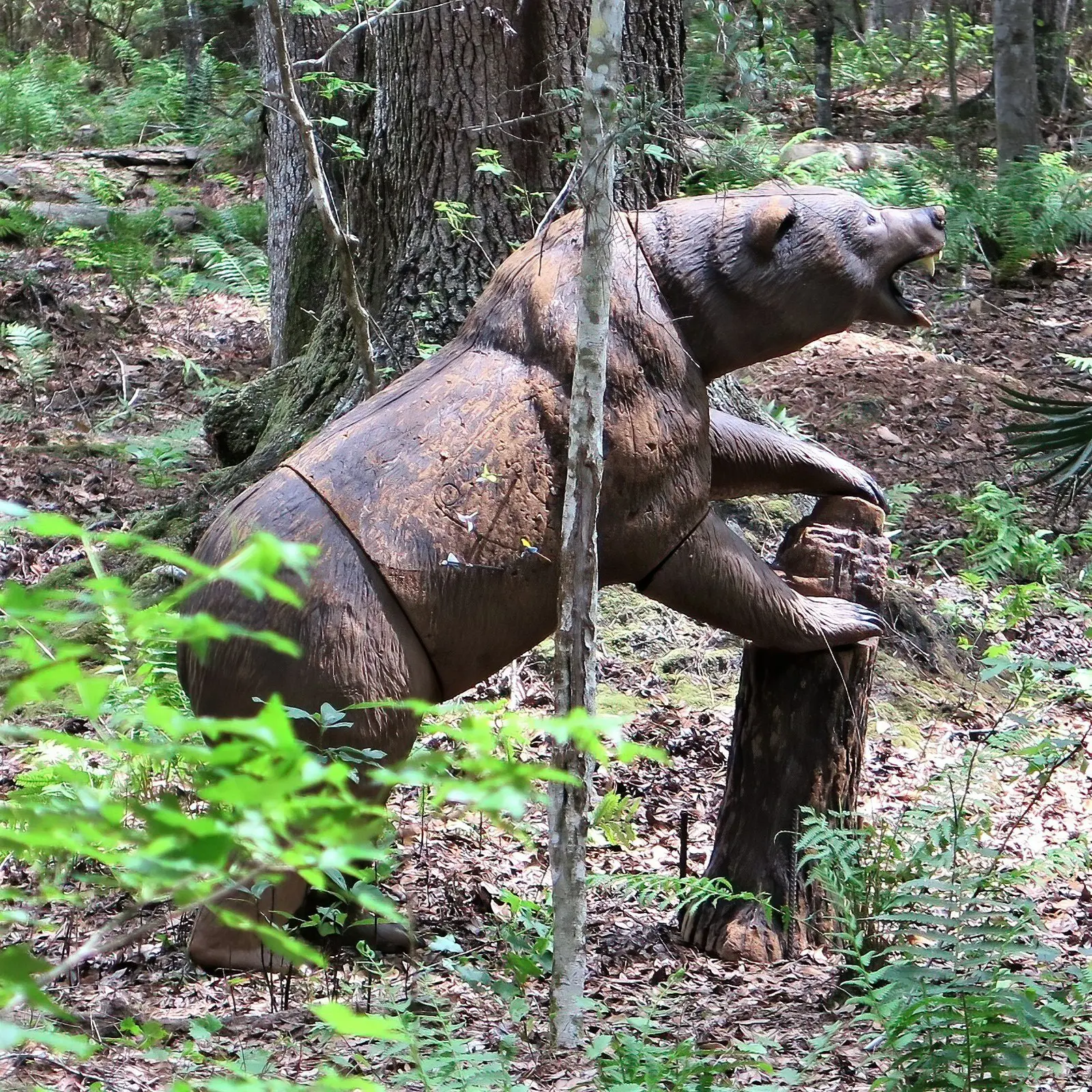 A rusty metal sculpture of a bear in a forest.