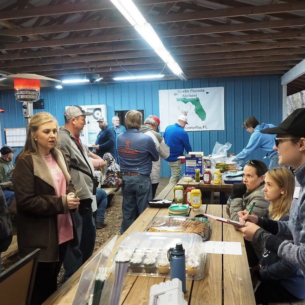 People gather around tables at an indoor event with various items on display.
